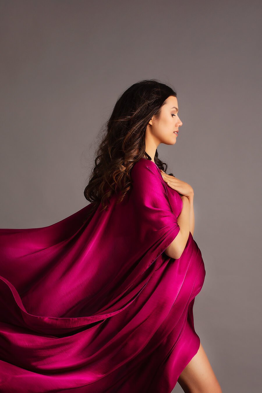 brunette model poses on her profile wearing a cherry silky cape.