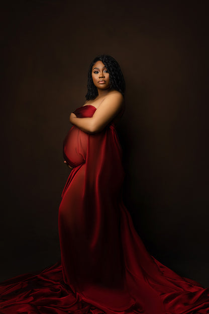 model with short dark hair poses in a studio wearing a bordeaux chiffon scarf to cover her body. the model is pregnant and staring at the camera. 