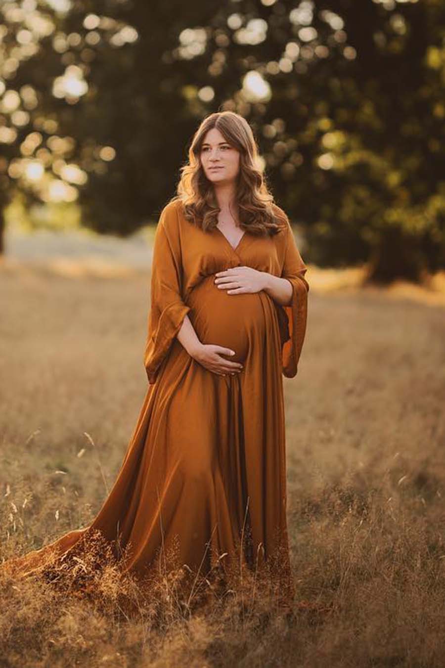 brunette model poses outdoors wearing a silky cognac long dress.