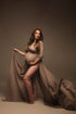 The pregnant woman is wearing a cape. The cape is made out of chiffon and has a espresso colour. In the same colour has she a rope around her right above her belly