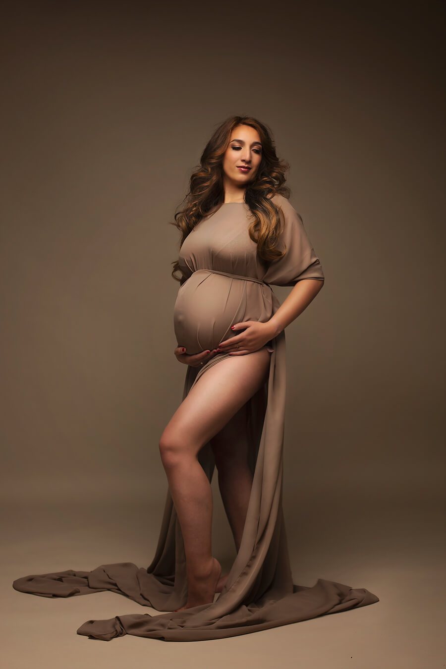 The pregnant woman is wearing a cape. The cape is made out of chiffon and has a espresso colour. In the same colour has she a rope around her right above her belly