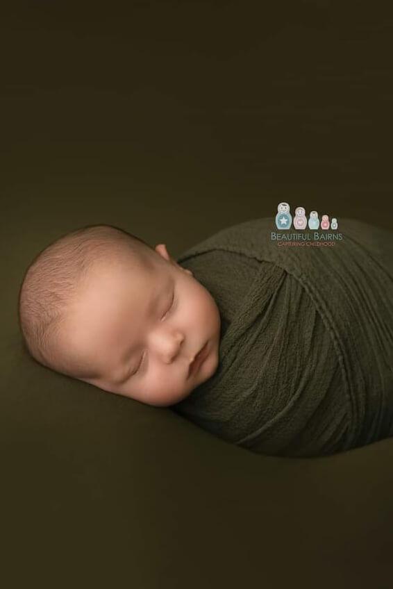 a baby is wrapped in a olive green fabric. The baby is sleeping