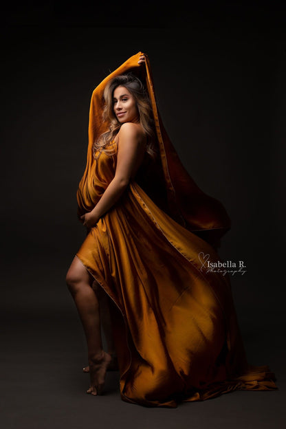 blond pregnant model poses with a cognac scarf covering her breast and belly. she holds a piece of the fabric above her head in a playful way.