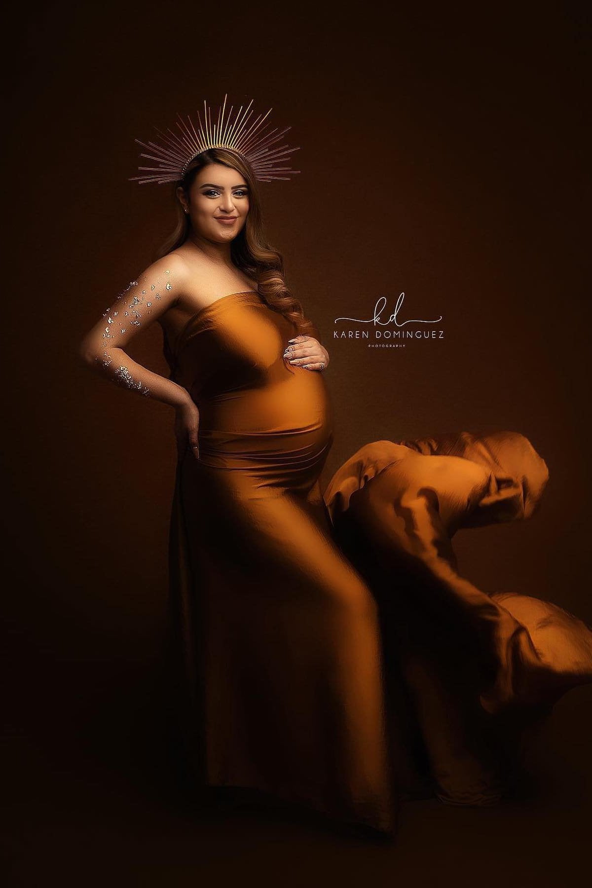 pregnant model poses with a cognac scarf around her body and a crown on her head. 