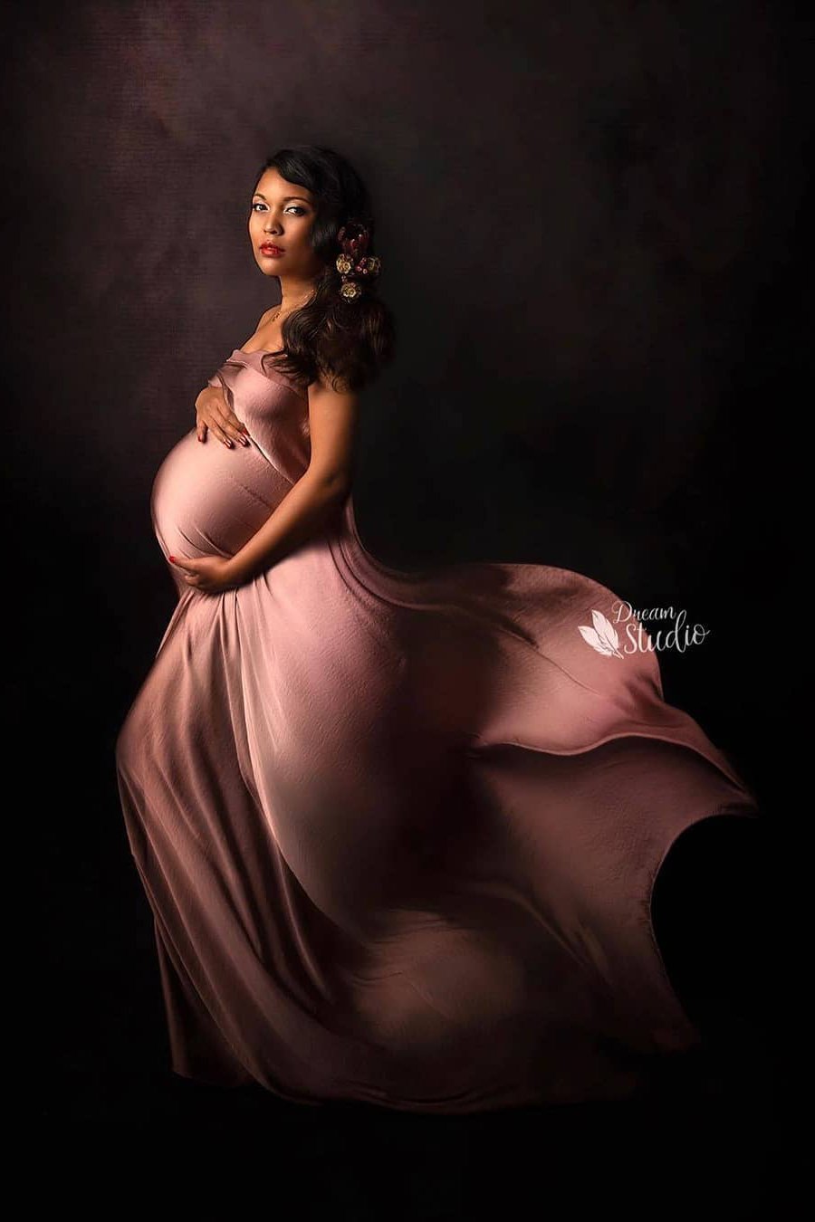 Brunette model poses on her side in a studio covering her body with a silky old pink draping fabric. 