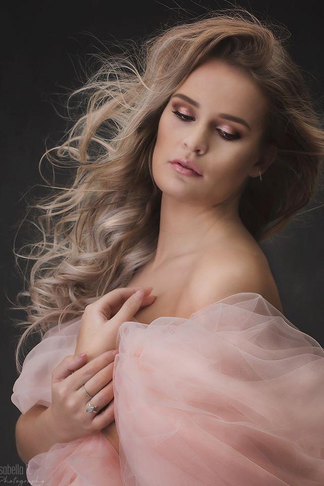 model poses in a studio for a maternity photoshoot wearing a tulle draping fabric in pink color.