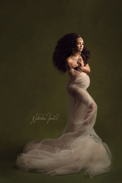 model poses in a studio for a maternity photoshoot wearing a tulle draping fabric in sand color.