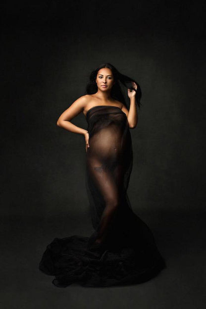 model poses in a studio for a maternity photoshoot wearing a tulle draping fabric in black color.