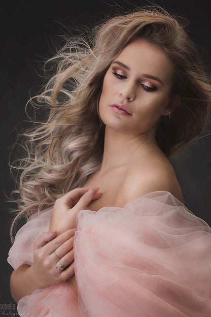 A blond model is holding her hands and has a Dusty pink tulle scarf around her. She is also wearing pink make up to finish the look