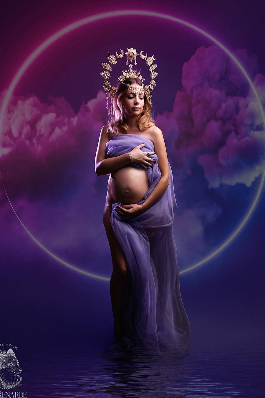 A pregnant woman is posing in front of a colorful background. The background has purple and pink clouds. It looks like she is standing in a small puddle of water. She is wearing the tulle scarf purple. She is holding up the fabric of the tulle and is looking down. The photograph has a magical look.