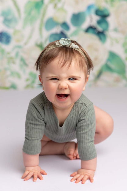 Baby poses in a studio wearing an azur long sleeved romper and a matching hair band.