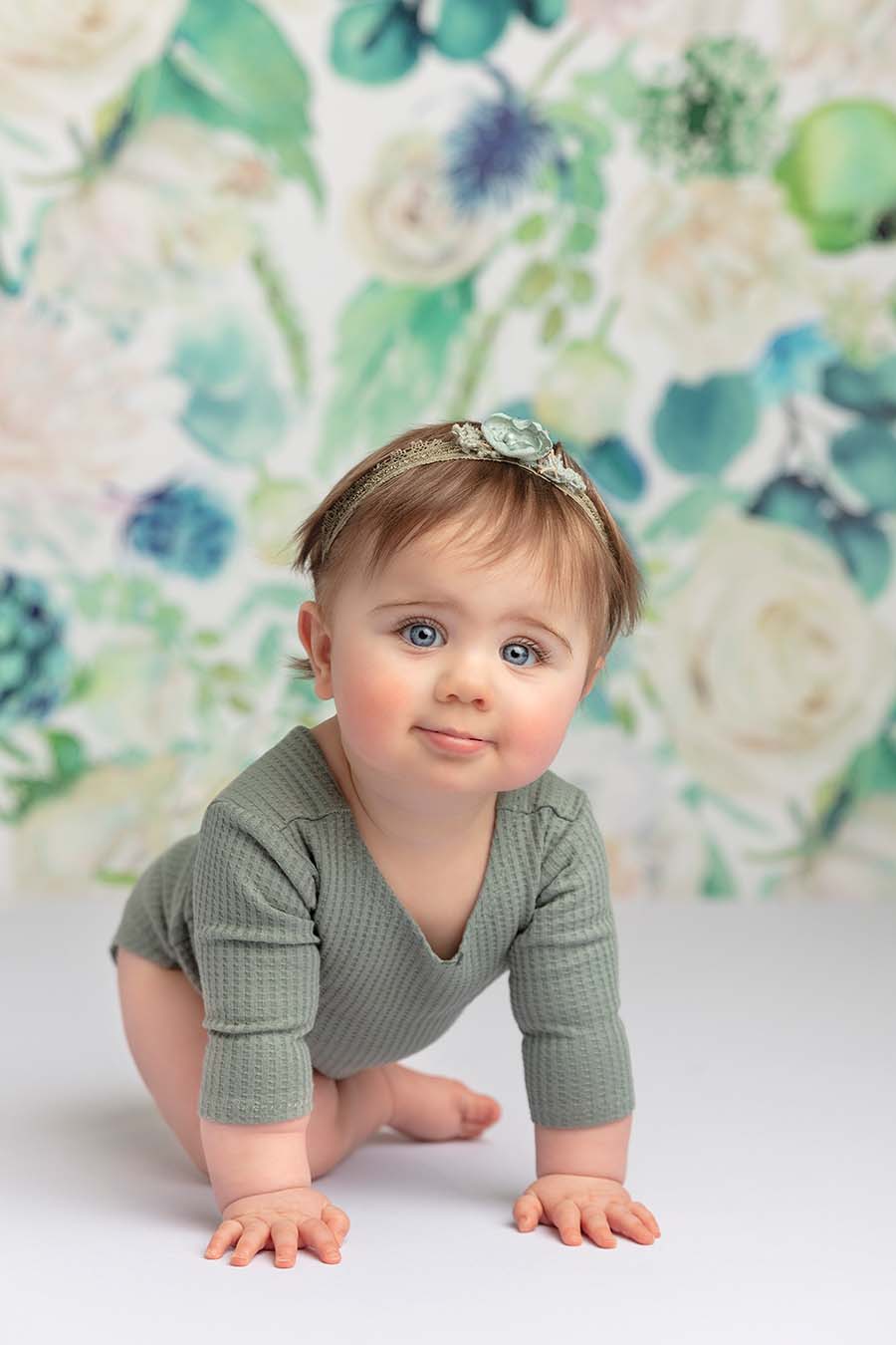 baby poses in a studio wearing an azur romper with long sleeves and a matching hair band. 