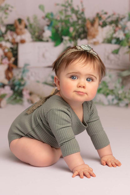 Baby poses in a studio wearing an azur long sleeved romper together with a matching hair band. 